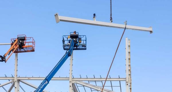 Crane lifting steel beams against a blue sky backdrop