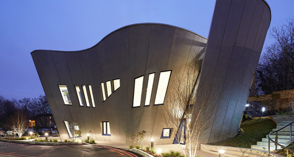 A night time view of Maggie's Centre, illuminated to highlight its unique architecture and create a welcoming ambiance.